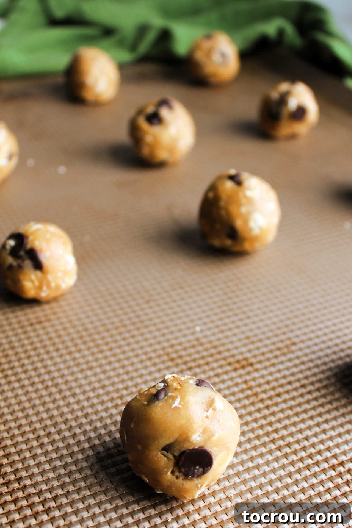 Scoops of cowgirl cookie dough rolled into balls and placed on baking sheet ready to go in the oven.