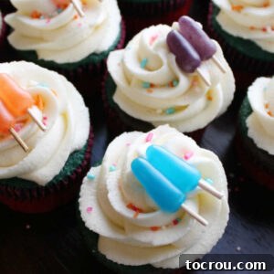 Close up of cupcakes topped with fluffy homemade frosting, sprinkles, and candies in the shape of popsicles.