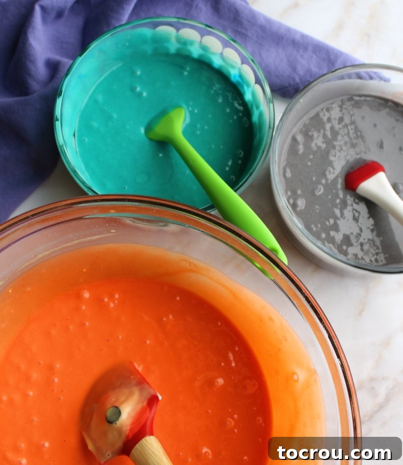 Separate bowls filled with vibrant pink, blue, and purple cupcake batter, ready for layering.