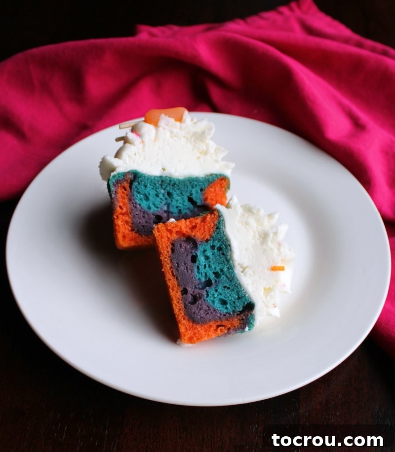 A vibrant summertime cupcake cut in half, clearly showing the distinct pink, blue, and purple colored cake layers.