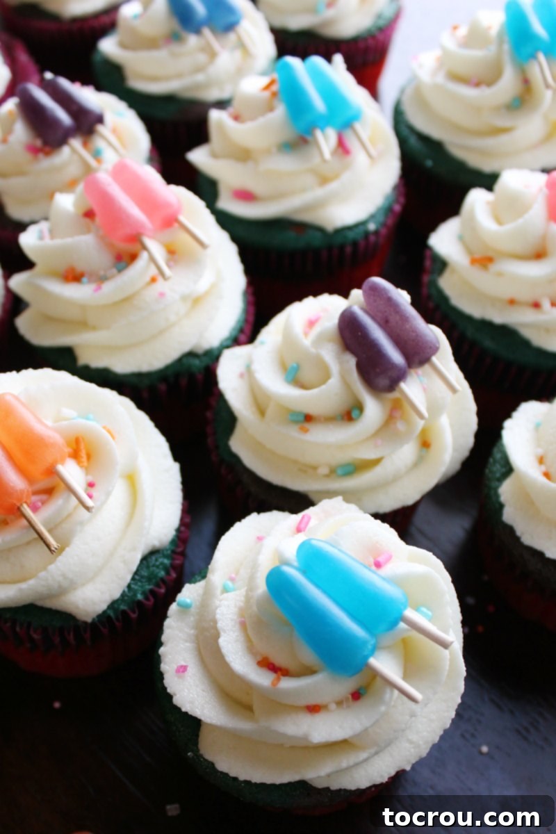 A vibrant assortment of sweet summertime cupcakes, each featuring elegant swirls of cream cheese frosting and delightful Mike and Ike popsicle toppers.