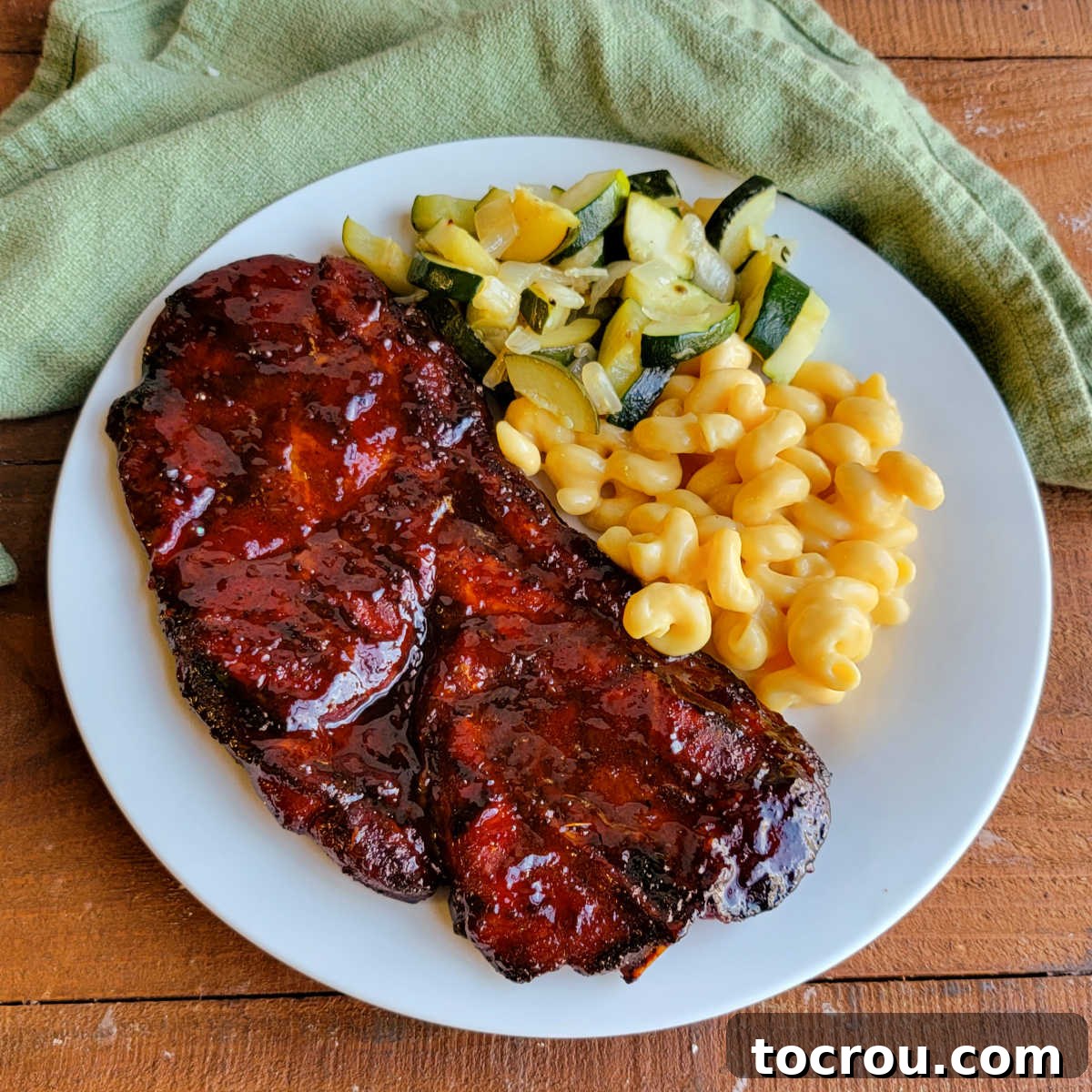 Smoky Perfection: Pellet Grill Pork Steaks 2 Dinner plate with a glossy bbq pork steak, macaroni and cheese, and sauteed zucchini.