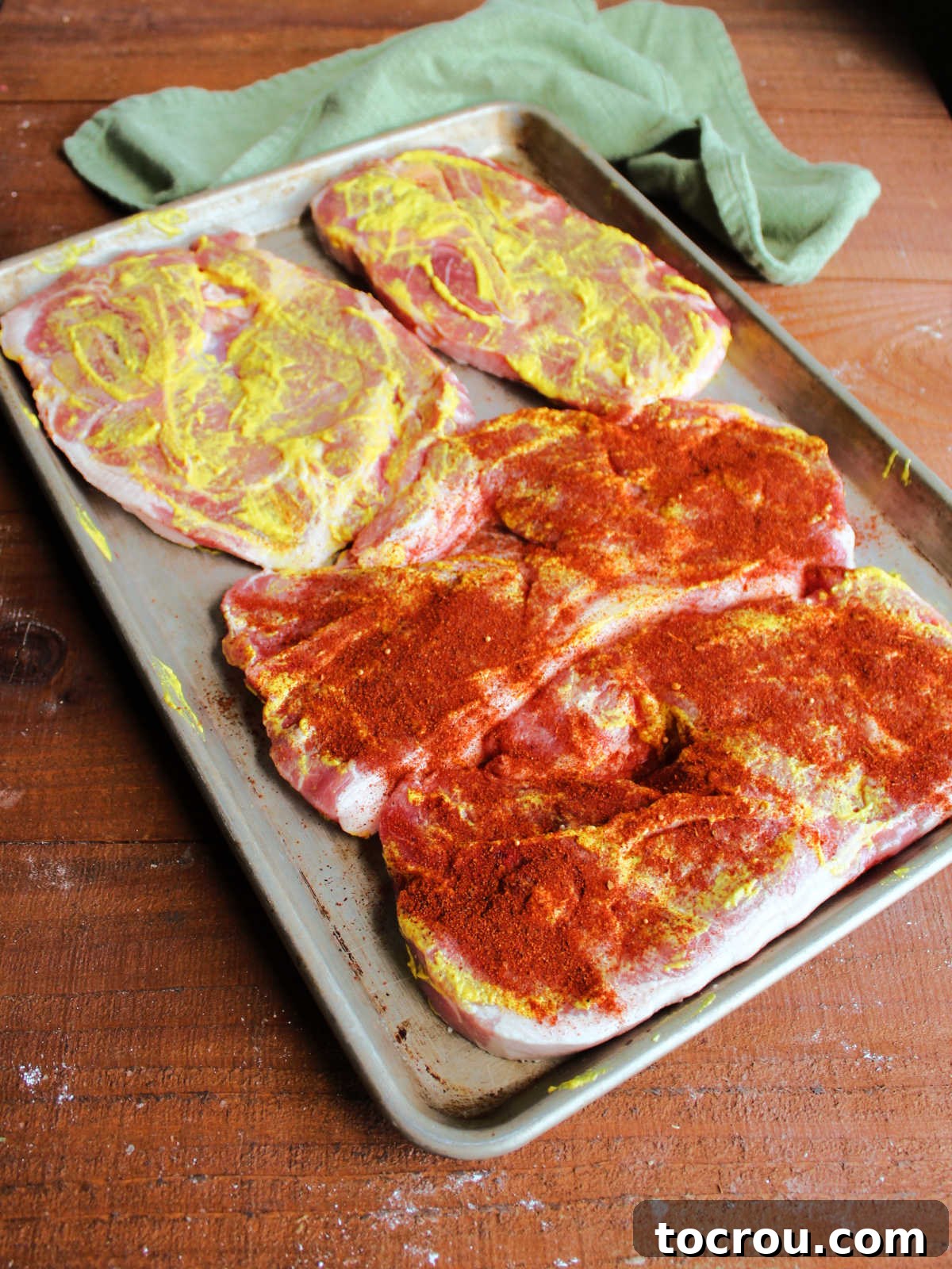 Smoky Perfection: Pellet Grill Pork Steaks 3 Pan of pork steaks coated in yellow mustard, two that have bbq rub on them and two that still need the rub applied.