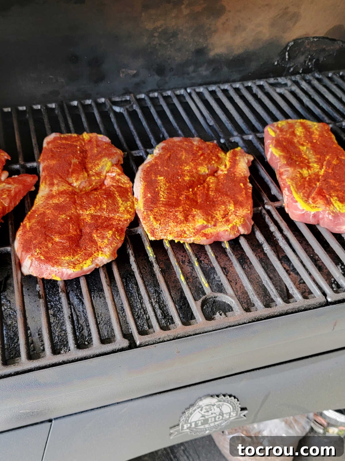 Smoky Perfection: Pellet Grill Pork Steaks 4 Pork steaks coated in mustard and dry rub on the smoker grates, ready to start cooking.