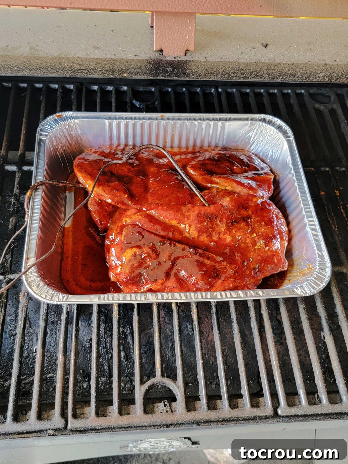 Smoky Perfection: Pellet Grill Pork Steaks 7 Second step of cooking, the smoked pork steaks are in an aluminum pan with bbq sauce, ready to cook more.