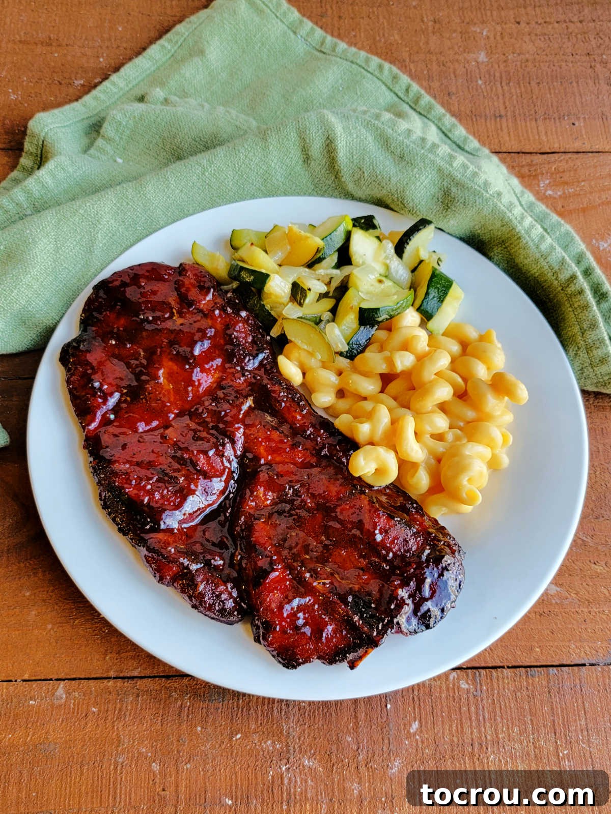 Smoky Perfection: Pellet Grill Pork Steaks 10 Plate with a large bbq pork steak, macaroni and cheese, and zucchini.
