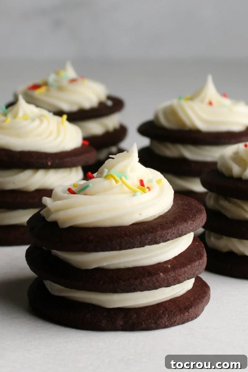 Stacks of dark chocolate cookies generously filled with piped cream cheese frosting between layers.