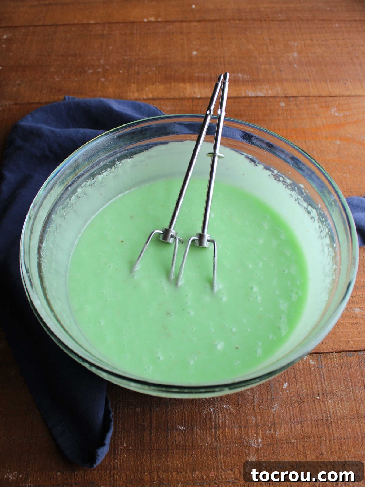 Mixing bowl with lime jello fudge mixture inside, the butter has melted and has been beaten in with a hand mixer so the mixture is thicker and has cooled some.