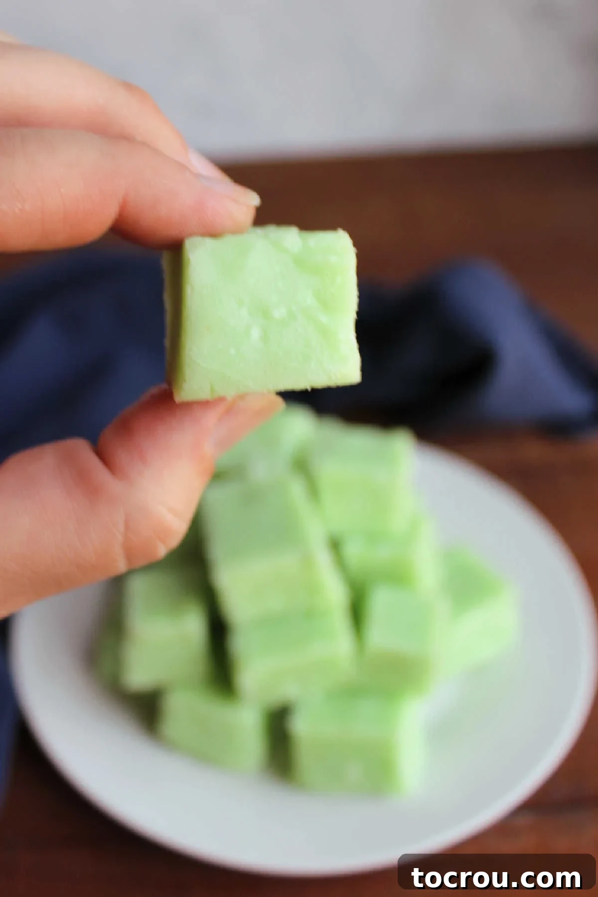 Hand holding a piece of lime jello fudge after it has been chilled to set and cut into squares.