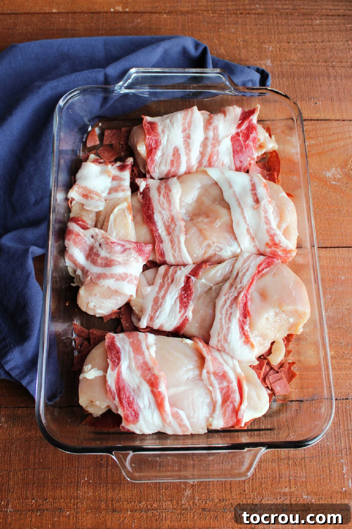 Bacon wrapped chicken breasts on top of chipped beef in pan.