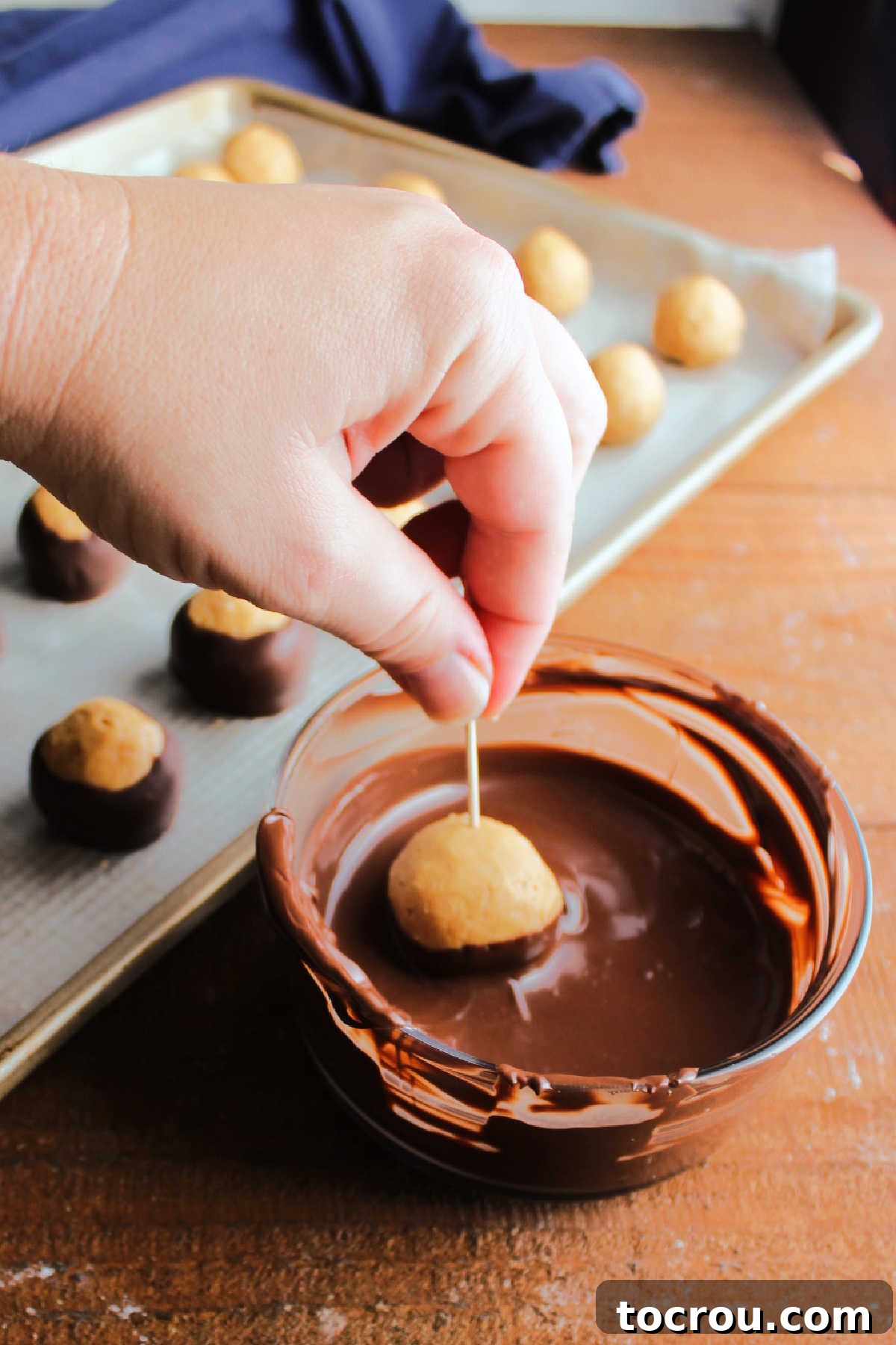 Rice Krispie Crunch Buckeyes 9 Hand dipping a peanut butter ball in melted dark chocolate using a toothpick to hold the peanut butter center.