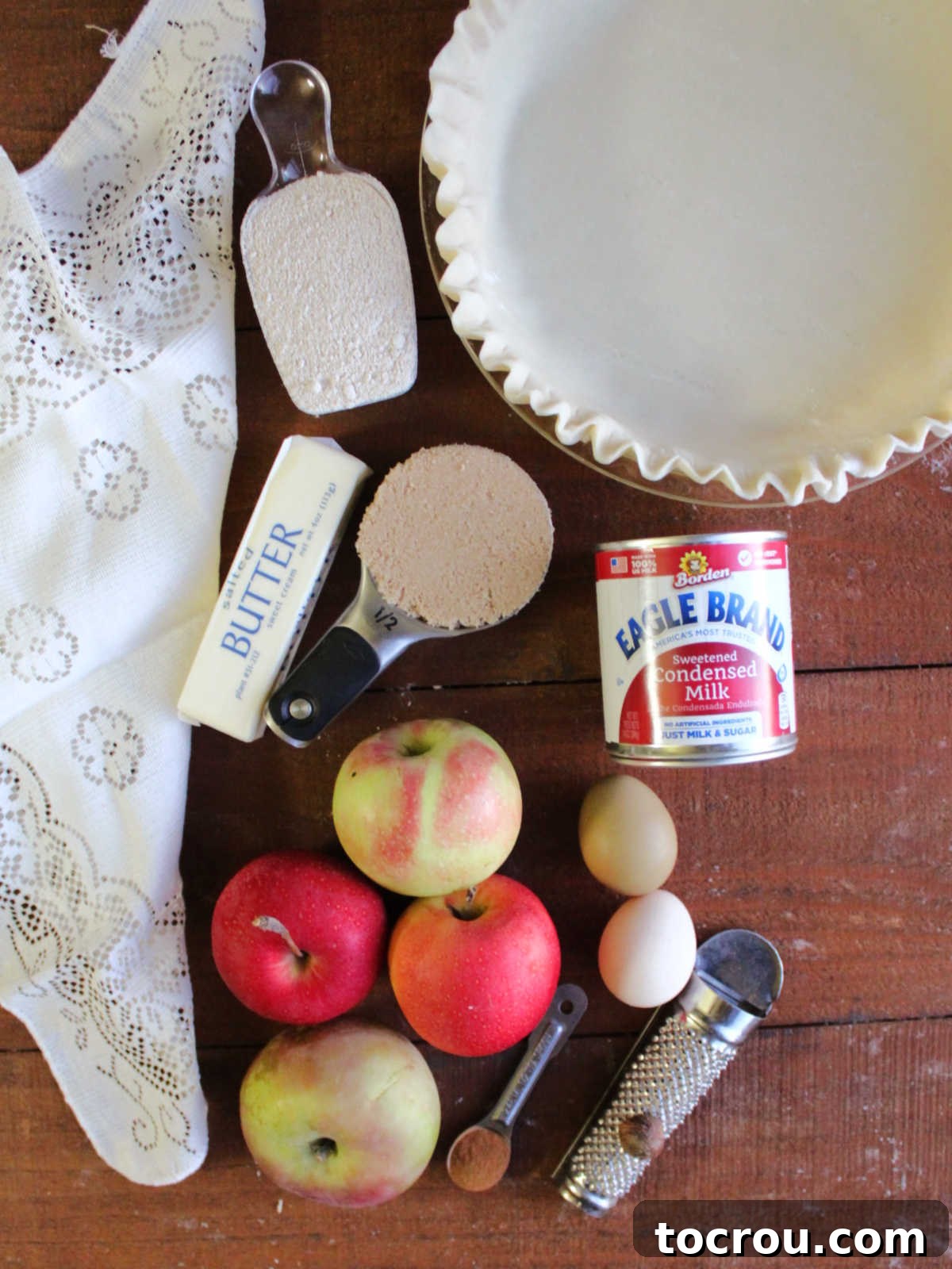 Apple Custard Crumble Pie 5 Ingredients including pie crust, apples, eggs, sweetened condensed milk, brown sugar, flour, butter, cinnamon and nutmeg ready to be made into pie.