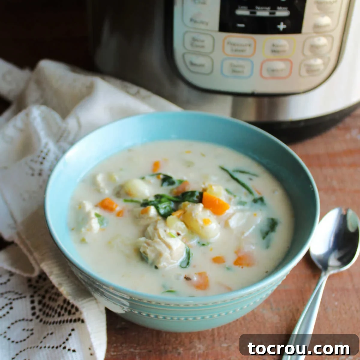 Bowl of creamy chicken gnocchi soup with carrots and spinach sitting in front of an Instant Pot.