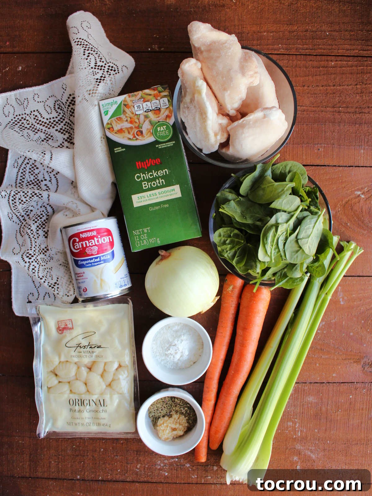 Ingredients including chicken, spinach, celery, carrots, onion, garlic, oregano, thyme, gnocchi, evaporated milk, and chicken broth ready to be made into soup.