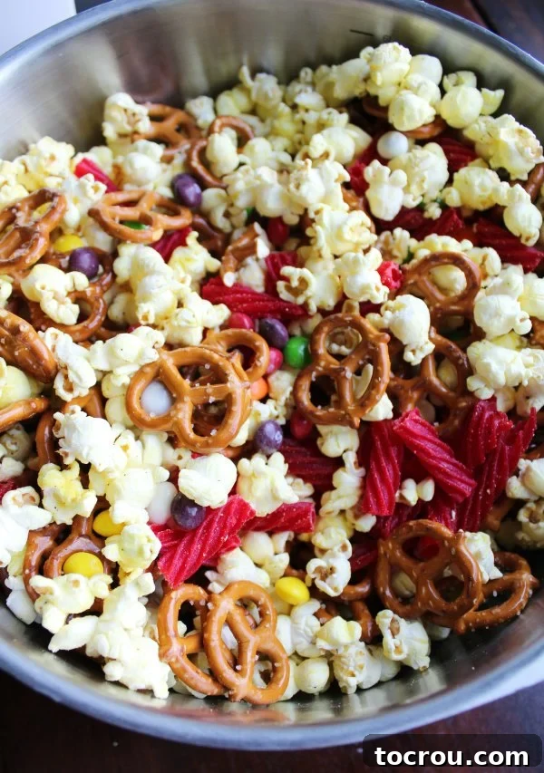 Large mixing bowl overflowing with popcorn, pretzels, and an assortment of colorful candies, ready to be combined into a snack mix.
