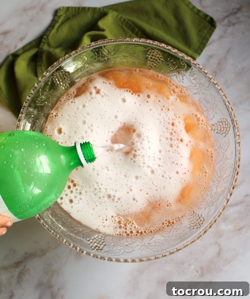 pouring white soda over slushy pink punch mixture in glass punch bowl.
