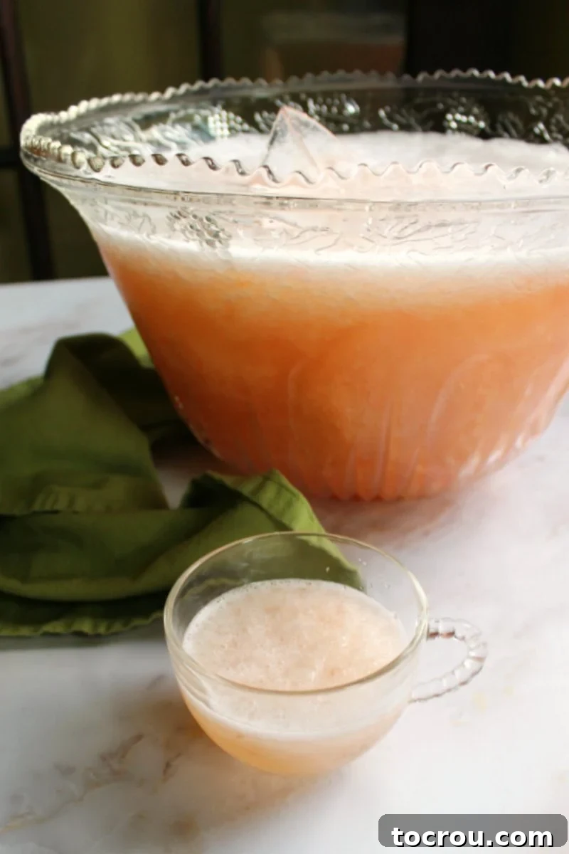 glass punch bowl full of slushy peach punch with a glass mug of punch in front of it.