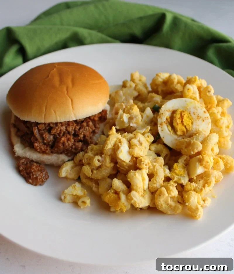 A hearty serving of homemade deviled egg pasta salad accompanying a classic sloppy joe sandwich on a plate.