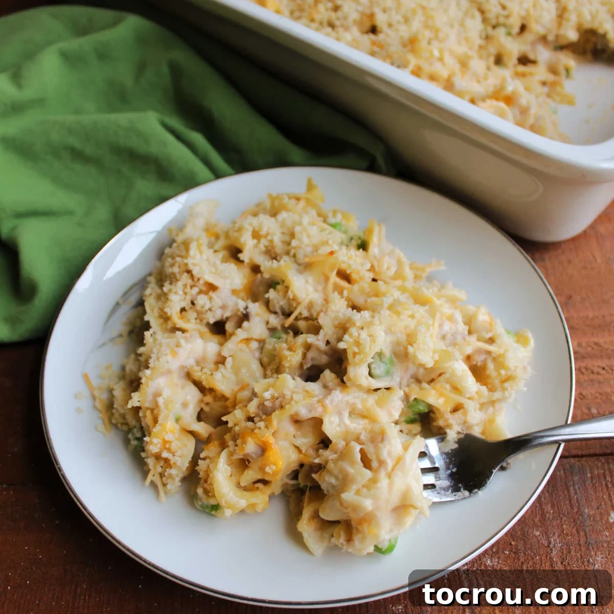 Hearty Tuna Noodle Casserole 2 Fork filled with creamy tuna noodle casserole, featuring peas, cheese, and crunchy bread crumbs, ready to be enjoyed.