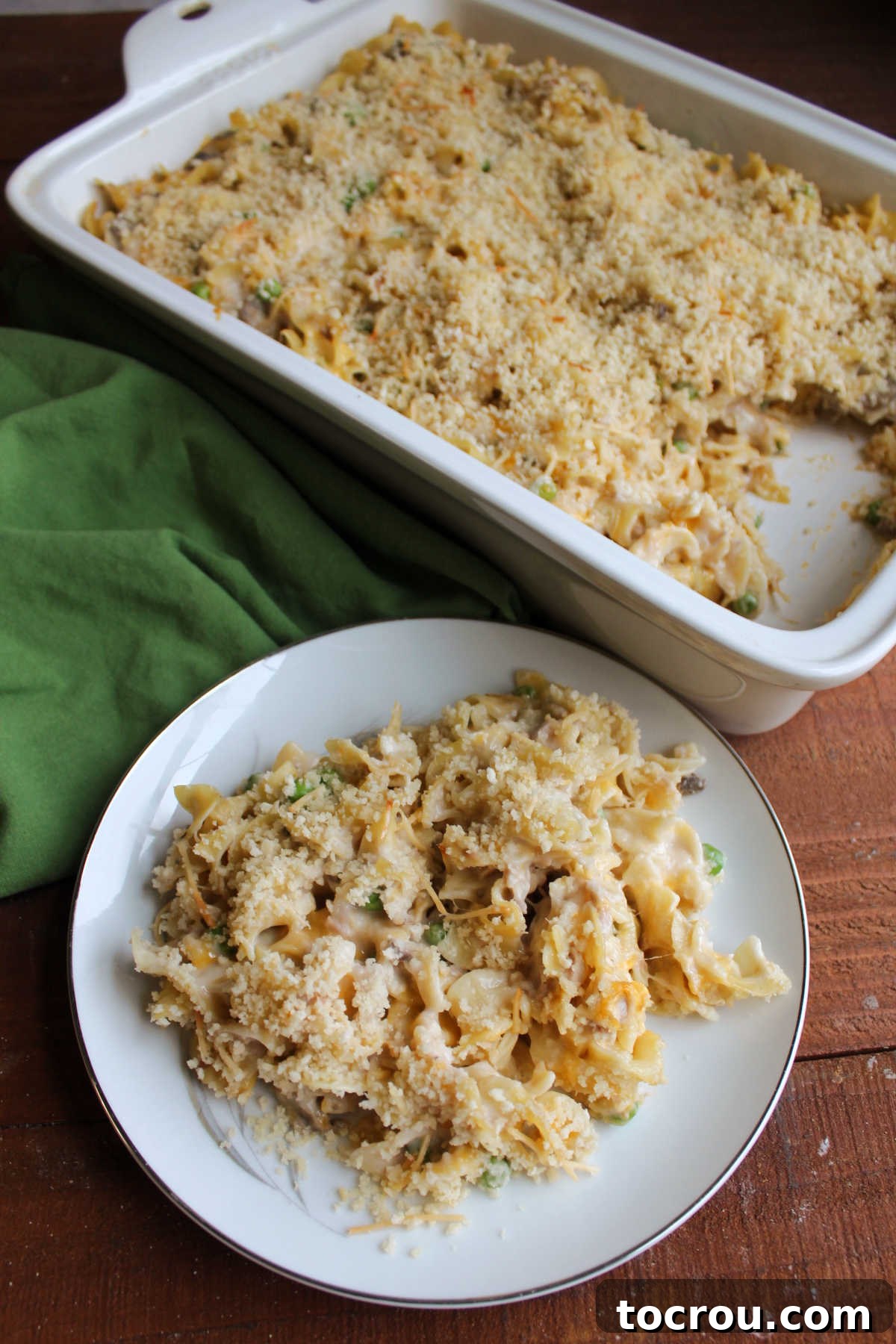 Hearty Tuna Noodle Casserole 11 Plate with a serving of tuna noodle casserole, showing its creamy texture and golden topping, positioned in front of the remaining casserole in the pan.