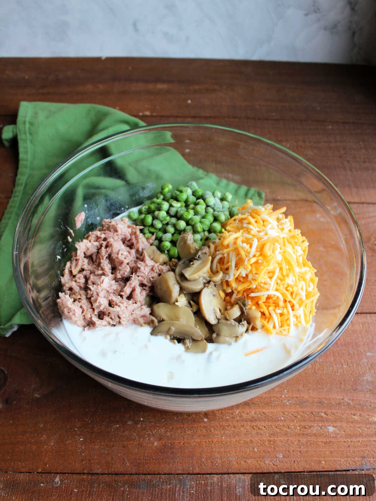 Hearty Tuna Noodle Casserole 4 Large mixing bowl with cream of mushroom soup and milk mixed together, topped with peas, Colby Jack cheese, and drained mushrooms.