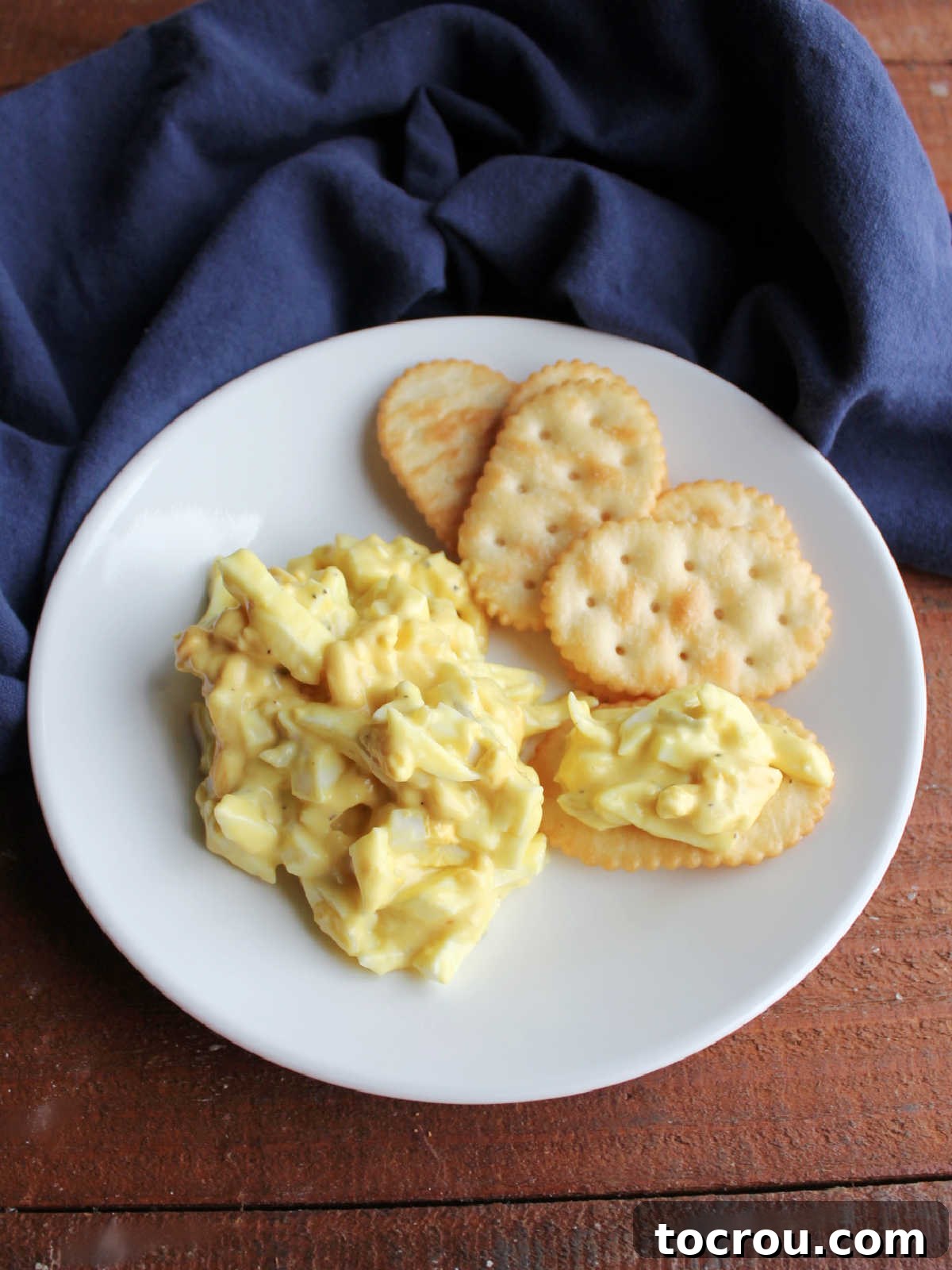 Pile of egg salad on small plate with butter crackers next to it.