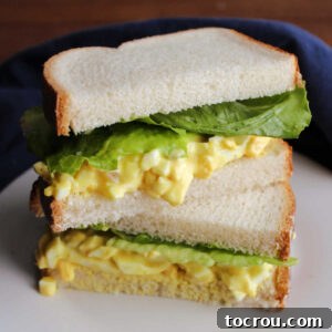 Egg salad sandwich with white bread, chunky yellow egg salad, and lettuce cut in half and stacked.
