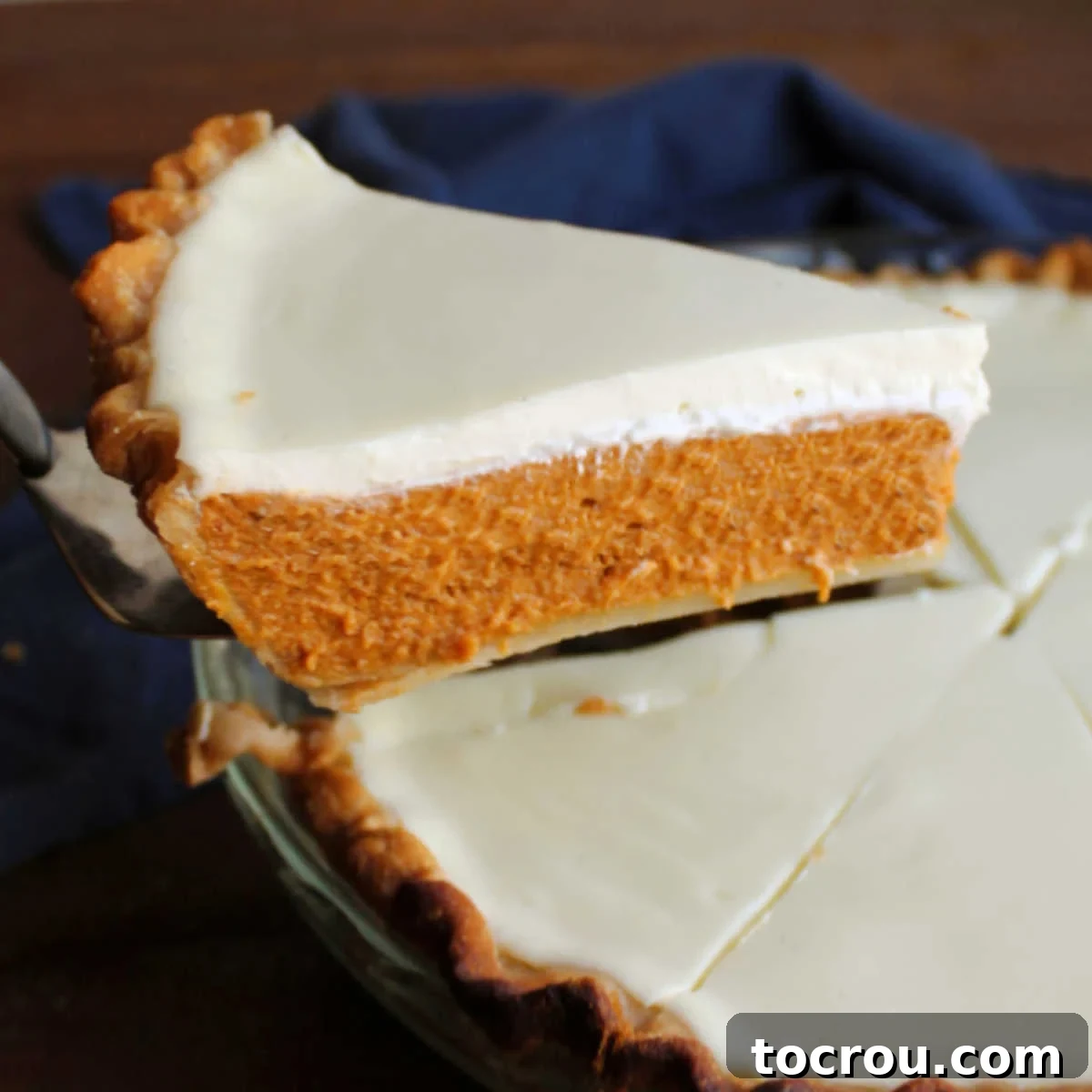 Lifting a slice of layered pumpkin pie from the pan, showcasing its rich condensed milk pumpkin pie layer topped with a smooth, creamy sour cream topping. Ideal for Thanksgiving.