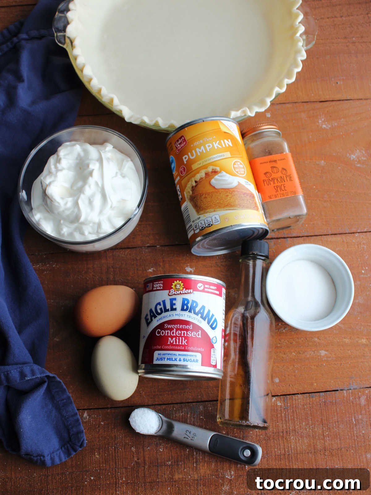All the essential ingredients for a layered pumpkin pie laid out: pie pastry, pumpkin puree, pumpkin pie spice, sugar, vanilla, salt, sweetened condensed milk, and sour cream.