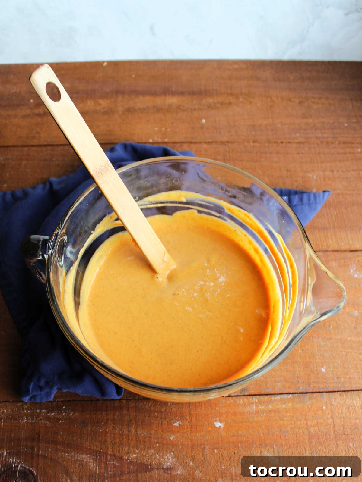 Glass mixing bowl filled with the smooth, orange condensed milk pumpkin pie filling, ready to be poured into the crust.