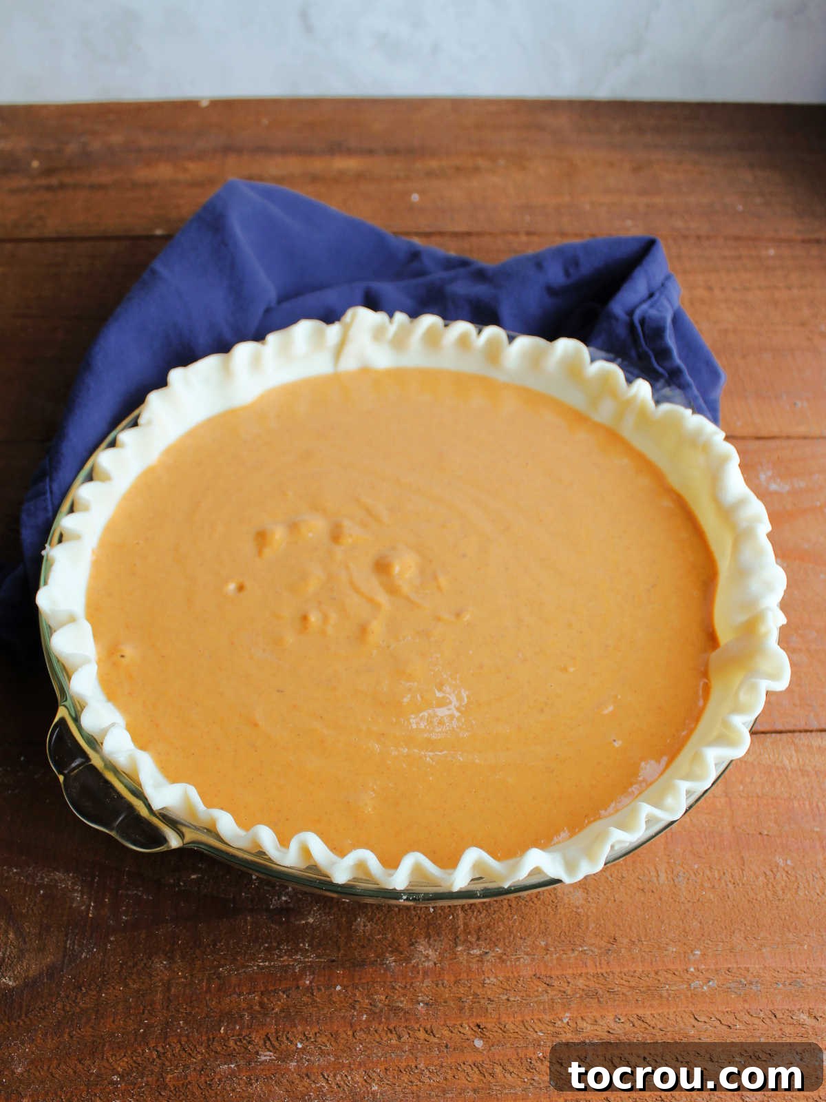 A pie dish containing a raw pie pastry, now filled with the vibrant condensed milk pumpkin pie mixture, awaiting its bake.