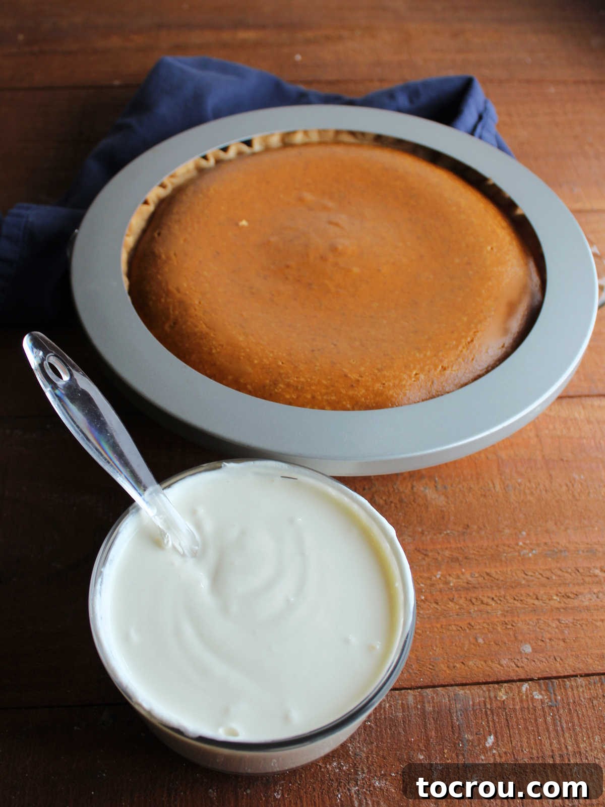 A small bowl holding the creamy mixture of sour cream, sugar, and vanilla, positioned in front of a partially baked pumpkin pie, ready for topping.