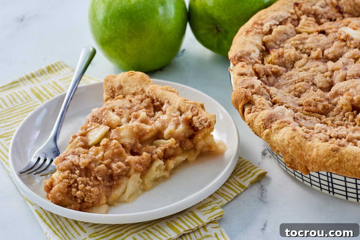Slice of grandma's dutch apple pie on plate with fork next to remaining pie. 