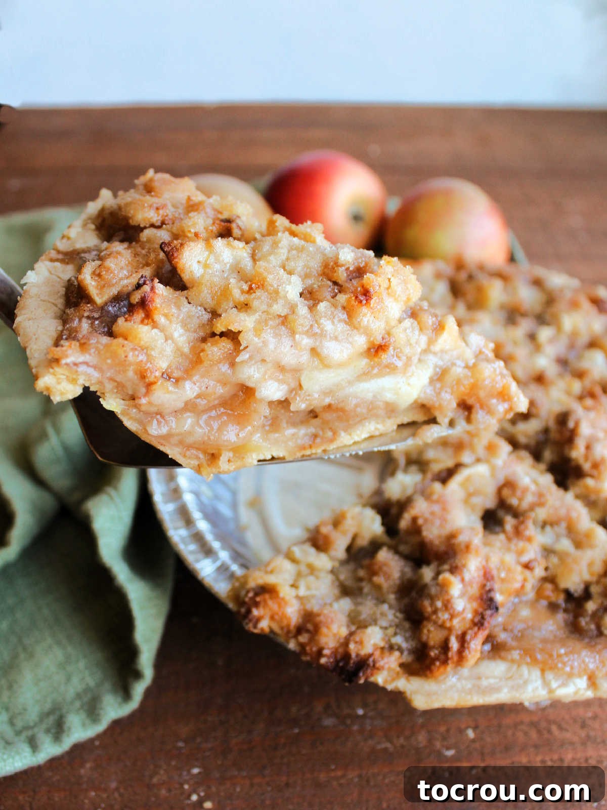 Pie server lifting out a slice of apple crumb pie with soft apple slices in the middle and buttery crumbs on top.