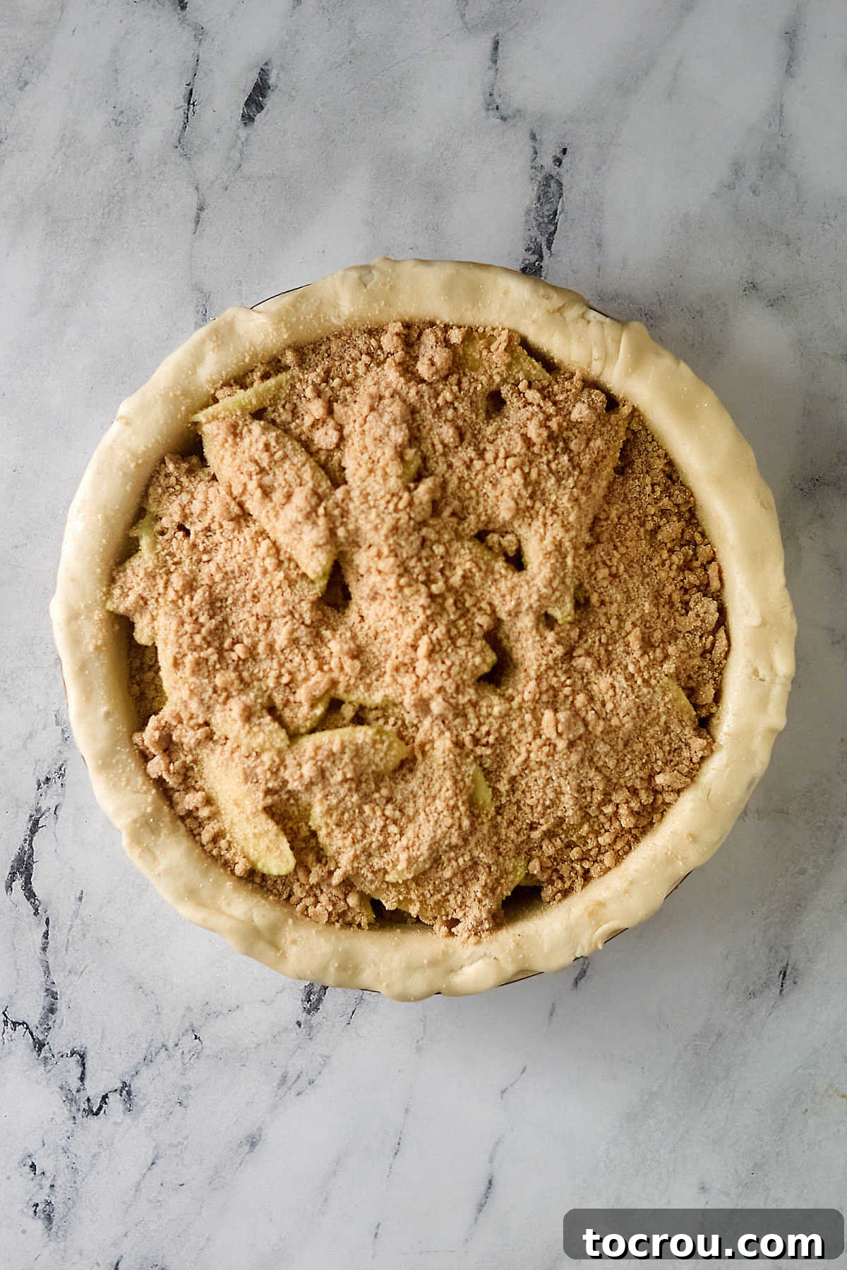 Pie crust filled with apple slices topped with buttery crumb topping, ready to go in the oven.