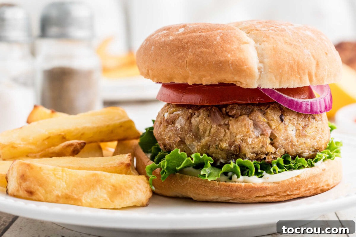 Homemade tuna burgers on bun with lettuce and onions served alongside french fries.