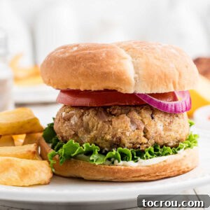 Tuna burger on bun with red onion and lettuce served with french fries.