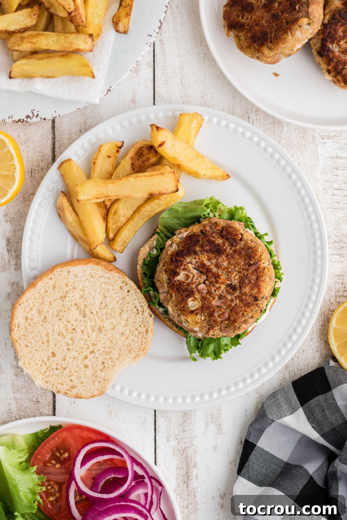Dinner plate with fries and a golden tuna burger placed on a bun, building the burger.