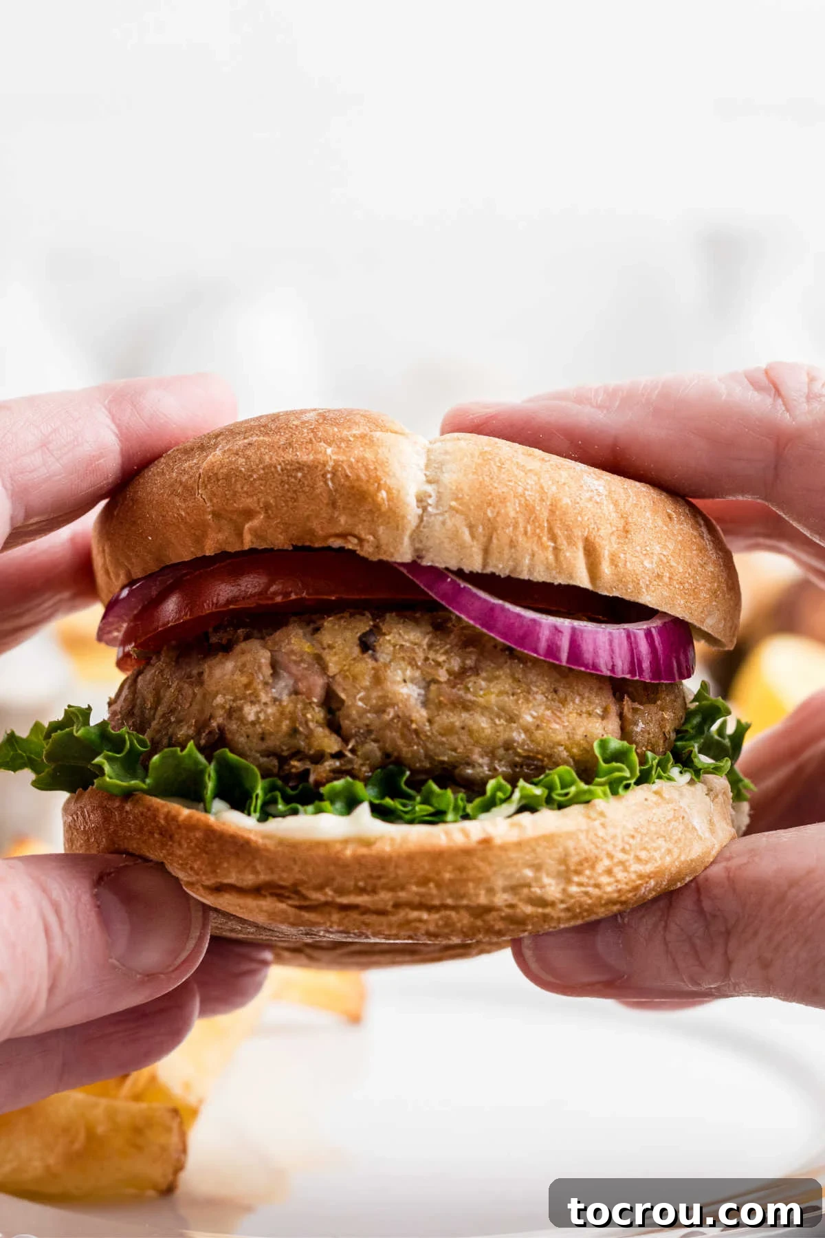 Hands holding tuna burger on bun with lettuce and red onion, ready to eat.