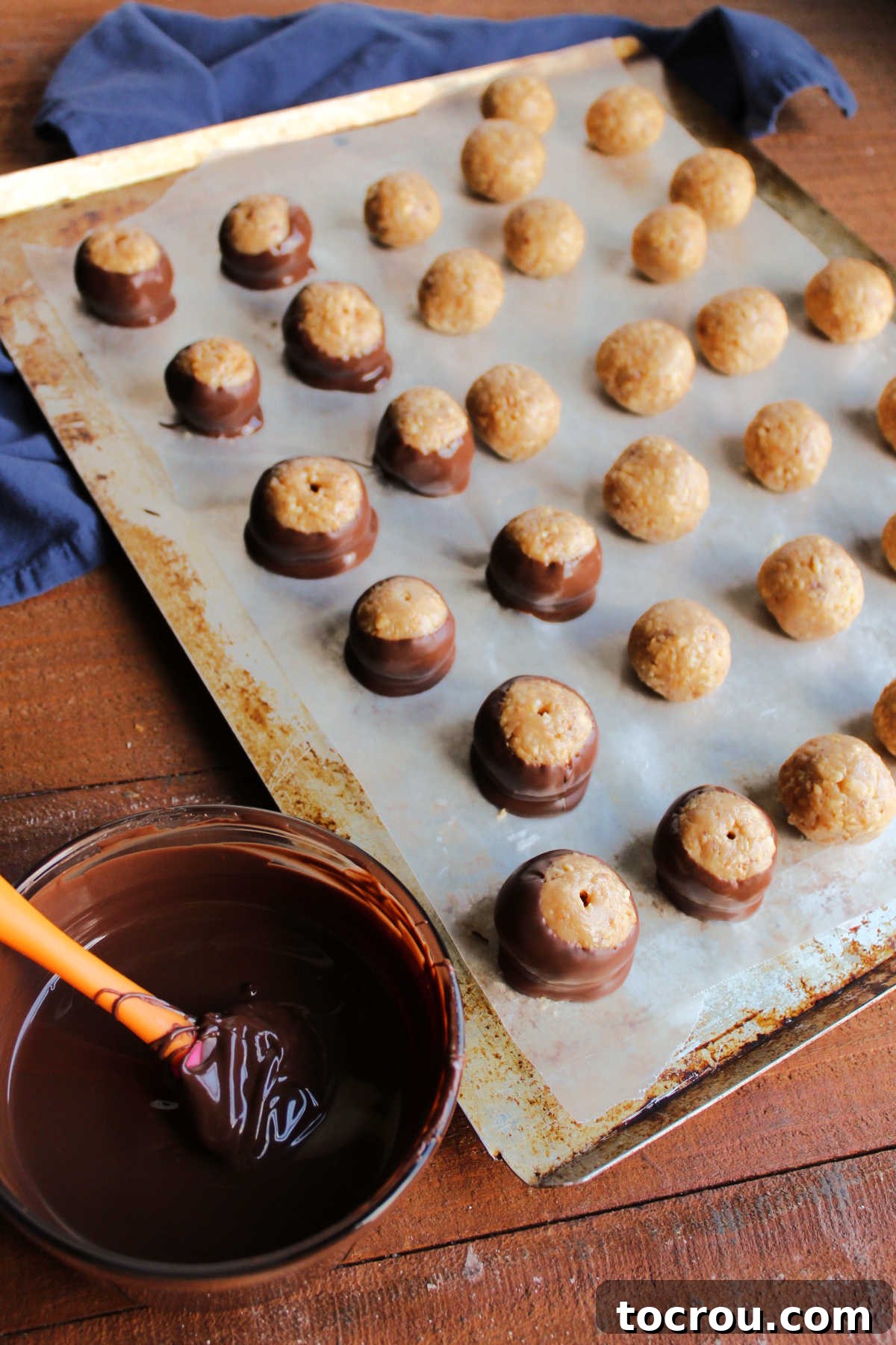 Dipping Caramel Peanut Balls in Chocolate A caramel peanut ball being dipped into melted chocolate with a toothpick, showing the smooth, glossy coating process.
