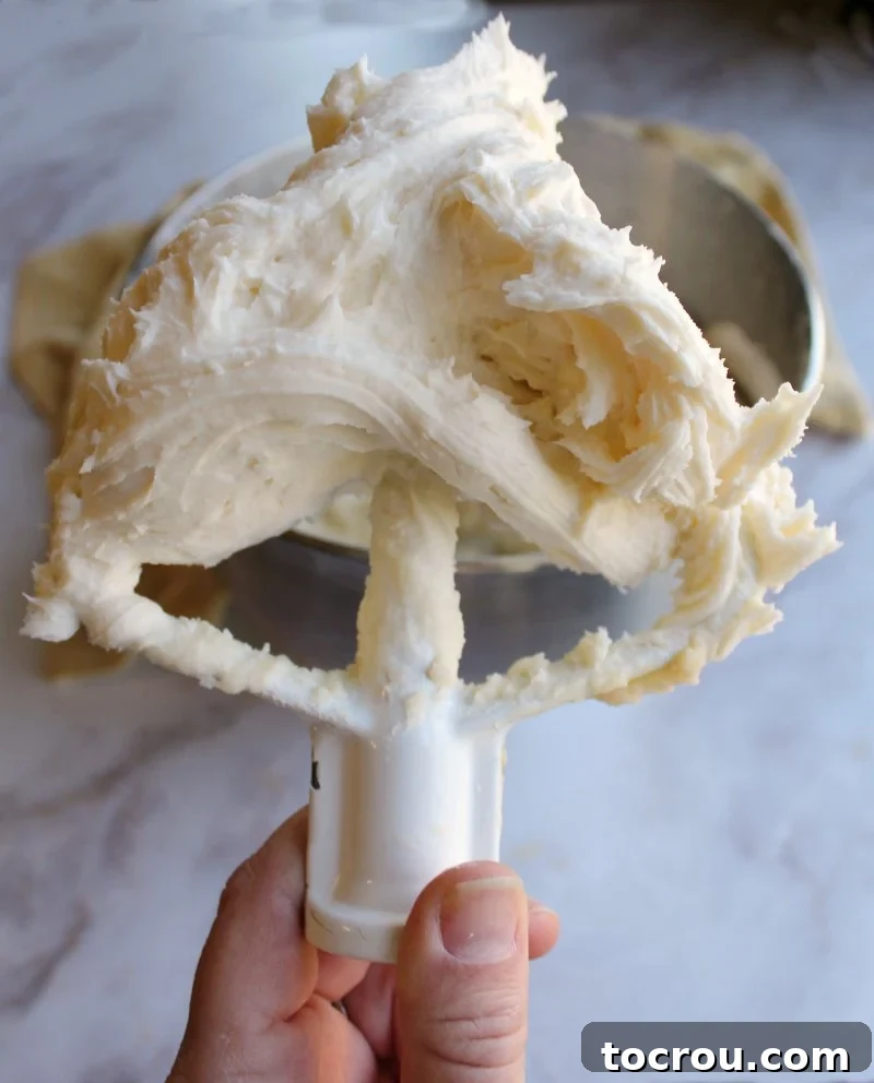 Sun-Kissed Lemon Honey Cream 2 A mixer paddle generously filled with smooth, pale yellow honey lemon buttercream frosting, ready for decorating.