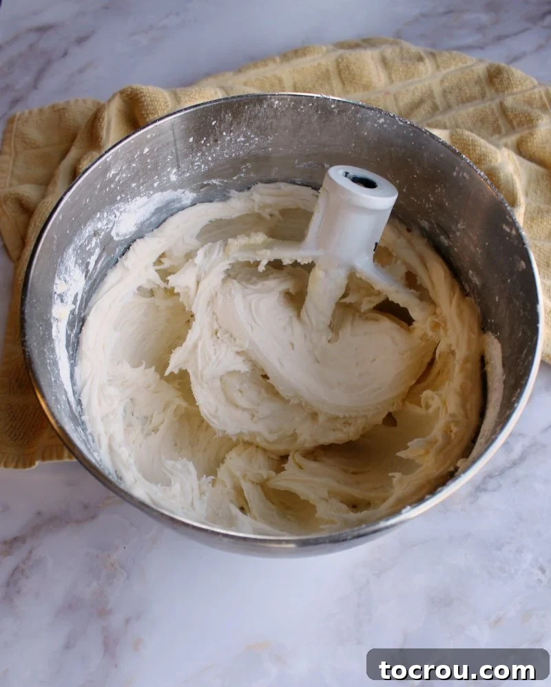 Sun-Kissed Lemon Honey Cream 5 A close-up shot of a mixer bowl brimming with fluffy, pale yellow honey lemon buttercream frosting.
