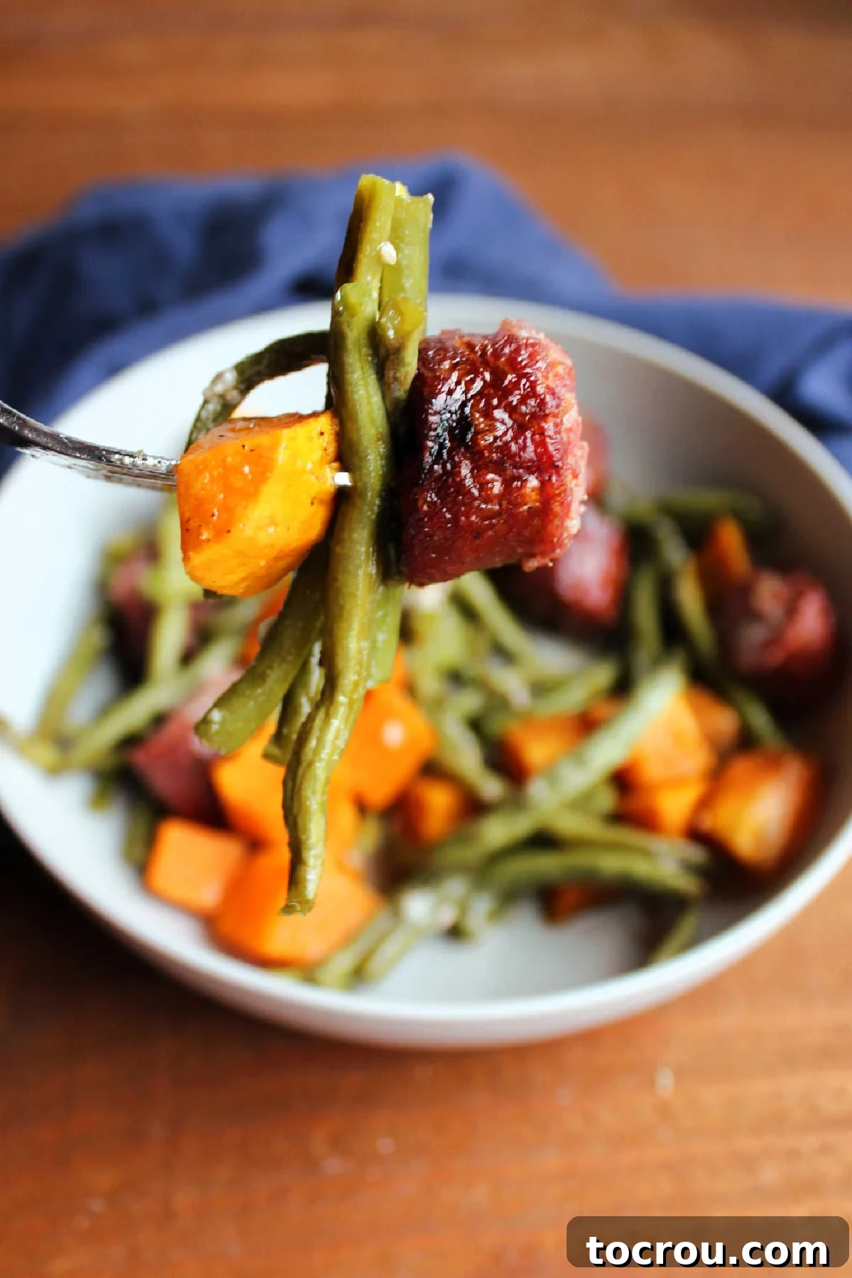 Bite of kielbasa, green beans and chunk of sweet potato on fork, showing roasted texture of each.