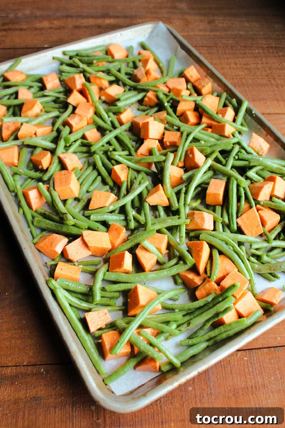 Trimmed green beans and sweet potato chunks tossed in oil and seasonings on sheet pan.