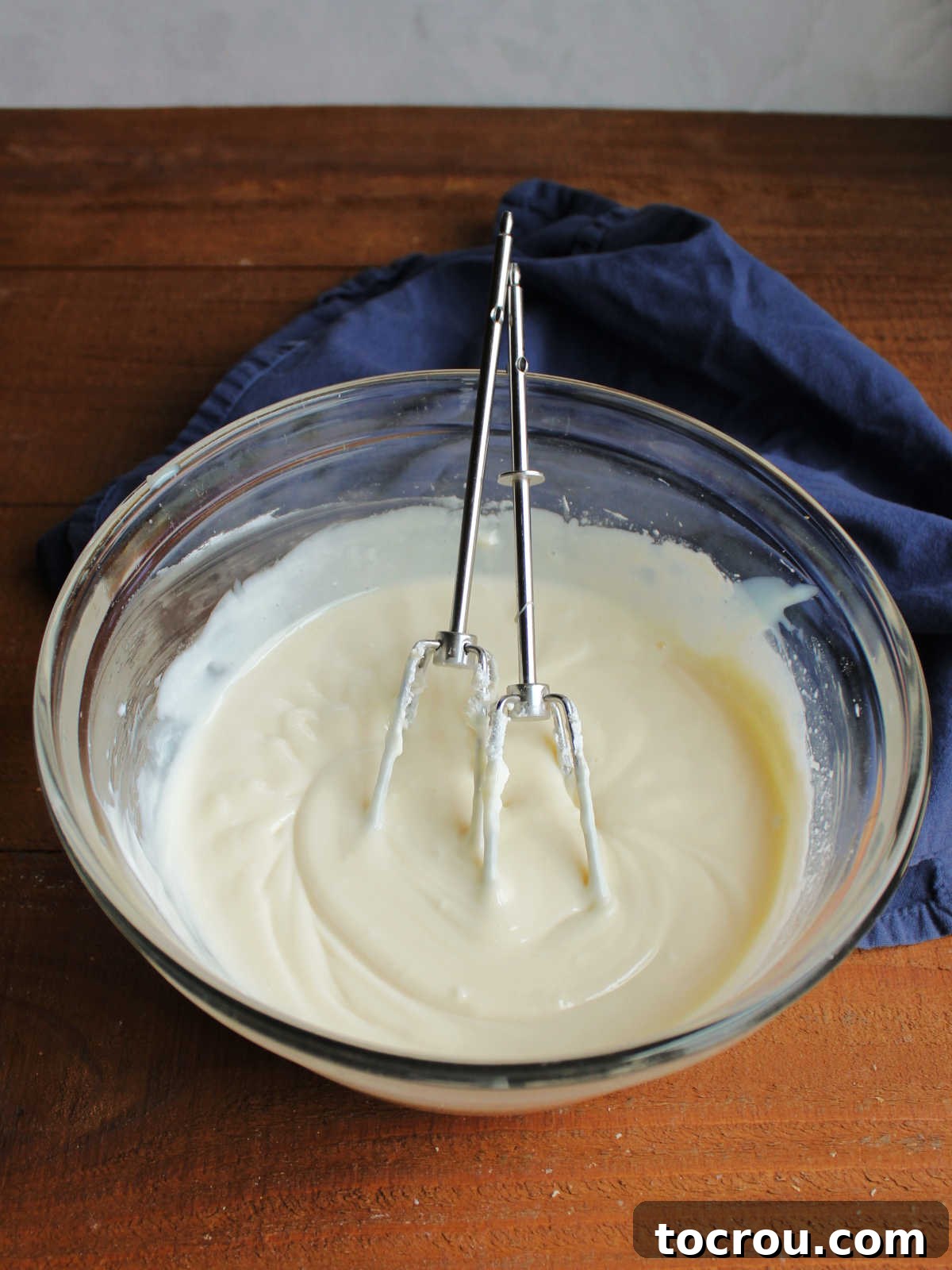 Buttery Crumb Cranberry Bliss 6 A mixing bowl filled with a smooth, creamy blend of cream cheese, sweetened condensed milk, and lemon juice, with hand mixer beaters visible, ready to be spread into the pie crust.