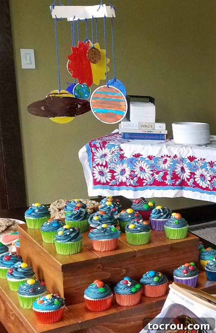 A display of solar system cupcakes on tiered cupcake stands, with a colorful, hand-colored planets mobile gracefully hanging above them.