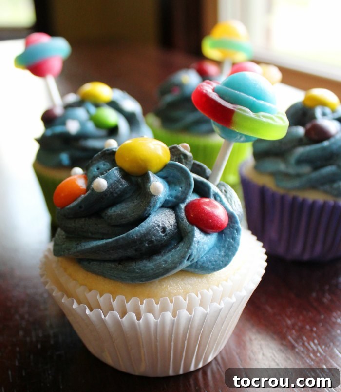 Close-up of cupcakes adorned with blue and black frosting, featuring candy planets and charming lollipop Saturns, ready for a cosmic celebration.