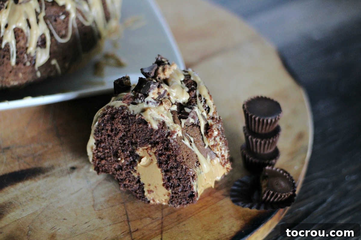 Enjoy the classic chocolate and peanut butter Reese's peanut butter cup combo in bundt cake form. This poke cake is easy to make and will leave a lasting impression! Slice of chocolate peanut butter poke bundt cake in front of remaining cake with stack of mini Reese's peanut butter cups nearby.