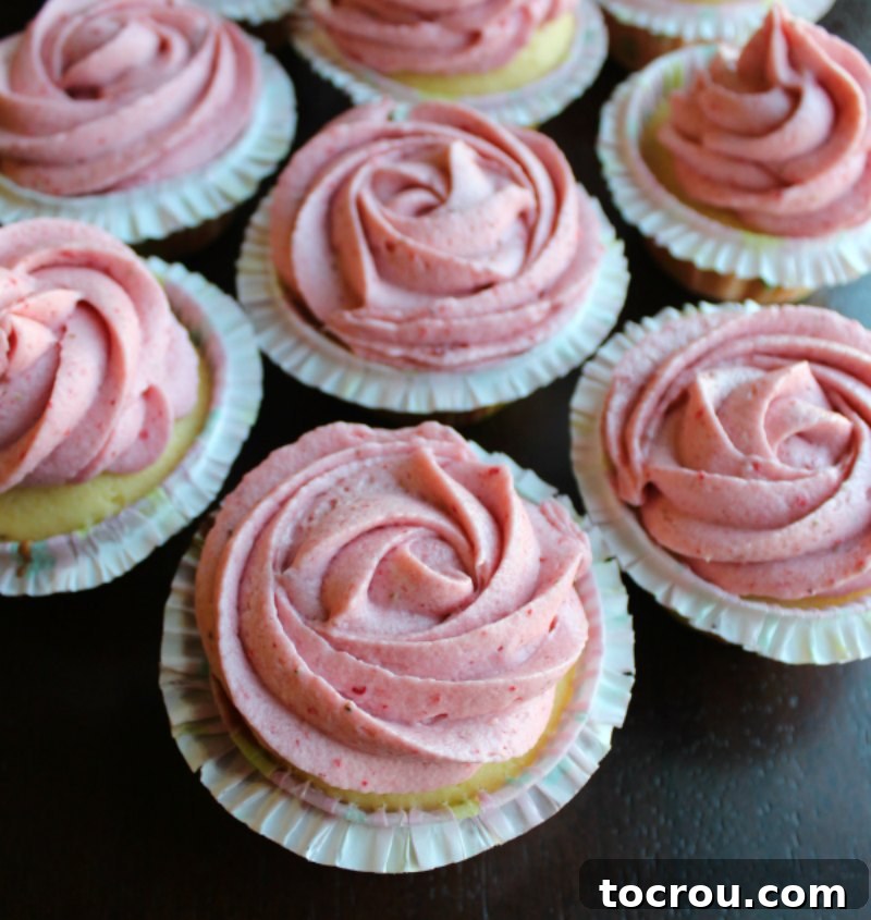 Vanilla cupcakes with rosettes of pink strawberry buttercream piped on top.