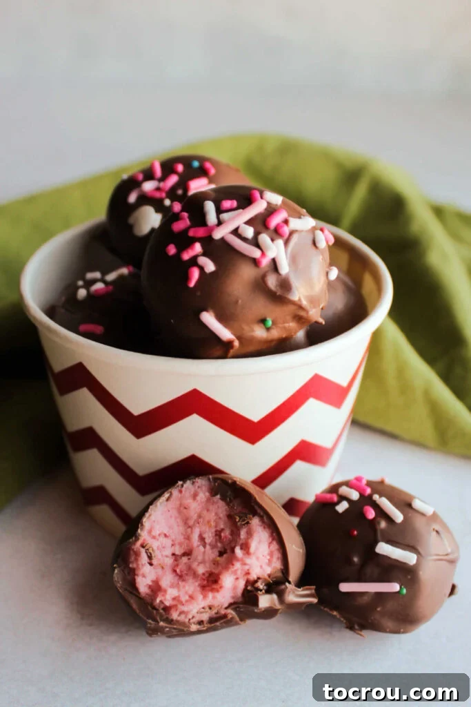 bowl of strawberry buttercream truffles topped with sprinkles with a bite taken out of one showing the soft pink center.